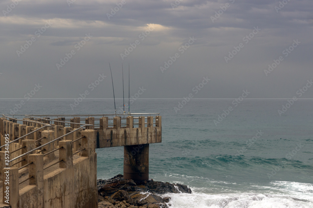 fishing poles on a concrete pier with the ocean in the background , no people