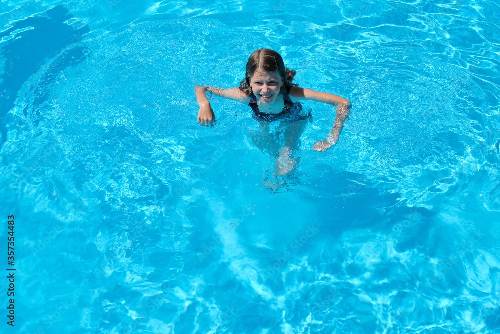 Kid has fun in an outdoor pool, child girl swims, dives, plays on the water, blue background