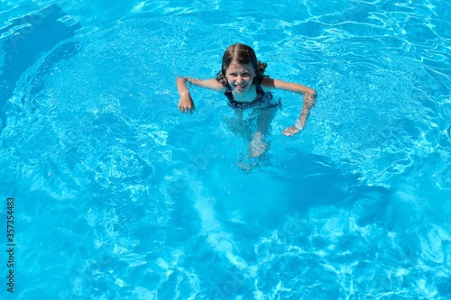 Kid has fun in an outdoor pool, child girl swims, dives, plays on the water, blue background