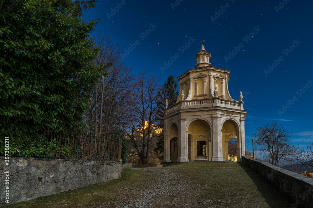 Sacred way in the moonlight. Sacro Monte di Varese, Italy, UNESCO site with the thirteenth chapel and the village of Sacro Monte illuminated on the left in the distance Sacred way in the moonlight. Sacro Monte di Varese, Italy, UNESCO site with the thirteenth chapel and the village of Sacro Monte illuminated on the left in the distance