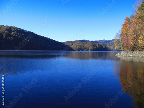 Scenic view of Nantahala Lake in the Smoky Mountains of North Carolina, USA. The coloured forest is reflecting in the water under a clear blue sky.