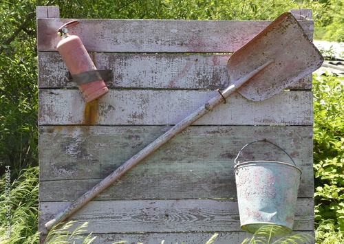 Fire extinguisher, bucket and shovel hanging on the board. Shabby and old