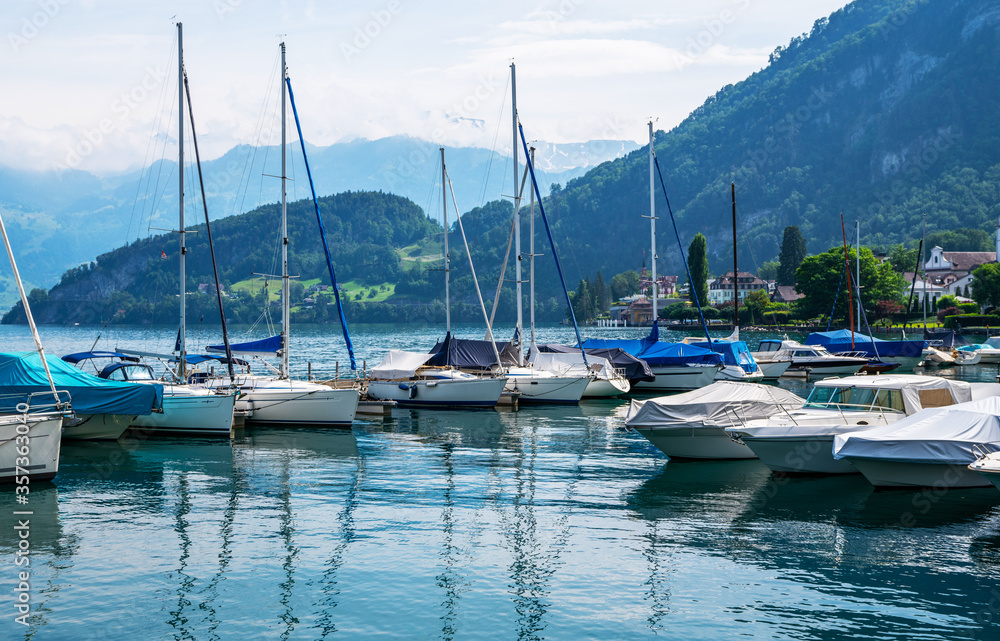 Early morning in harbor. Сoastal town Gersau of Lake Lucerne and Swiss Alps. A lot of white boats and luxury yachts moored in marina on a turquoise water, during a summer season. Travel and vacation.