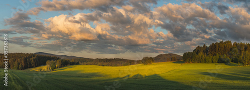 beautiful sunset landscape with meadows, trees, forests, in the background wooded hills and blue sky with clouds