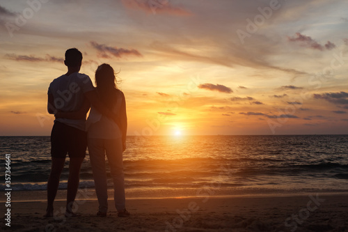 silhouette of young couple hugs on beach at orange sunset backside view copyspace