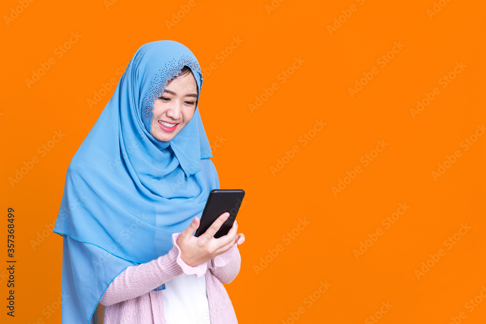 Smiling Asian muslim woman with using mobile or smartphone over isolated color background. Smiling Asian muslim woman with using mobile or smartphone over isolated color background.