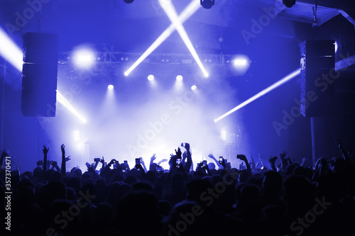 atmosphere of a cool music festival with a light-flooded stage and a full crowd hall. silhouette of musicians at a concert for a banner