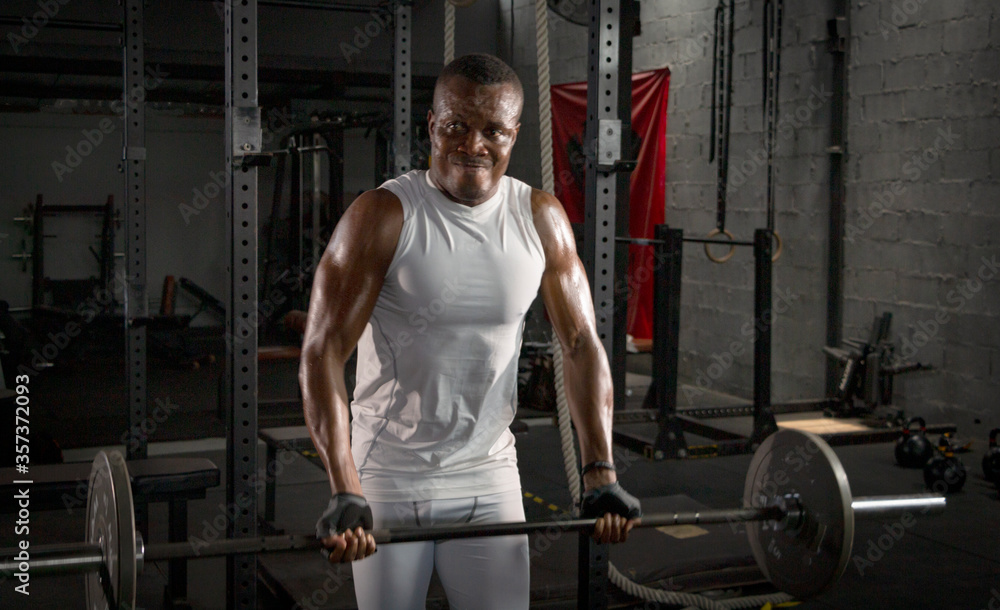Selective focus of young African athlete is doing exercise to build his biceps in a dark gym alone. African American man workouts by himself with dumbbell in shadow tone background Selective focus of young African athlete is doing exercise to build his biceps in a dark gym alone. African American man workouts by himself with dumbbell in shadow tone background