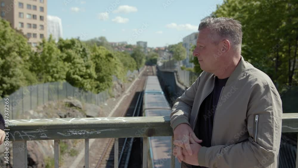 A middle-aged man talking on a bridge over the subway. A middle-aged man talking on a bridge over the subway.