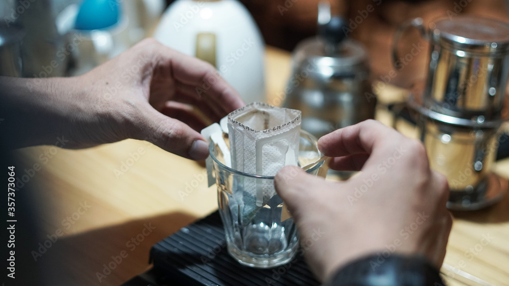 hand of barista preparing instant coffee drip on empty cup inside coffee shop bar