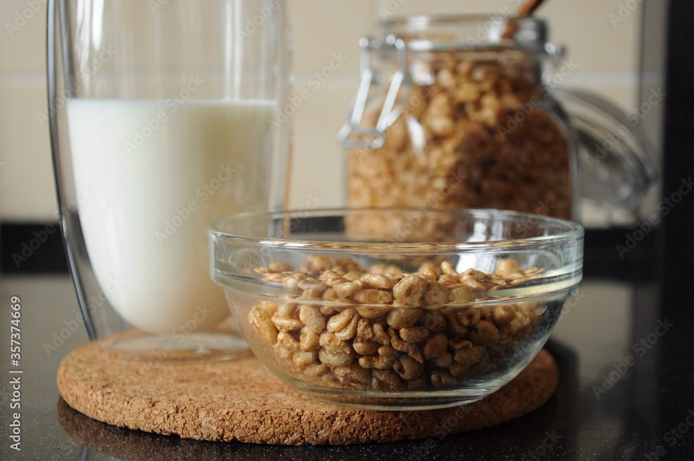 Breakfast from a bowl of wheat cereal, a glass of milk and a can of wheat cereal in the background on a cork stand Breakfast from a bowl of wheat cereal, a glass of milk and a can of wheat cereal in the background on a cork stand
