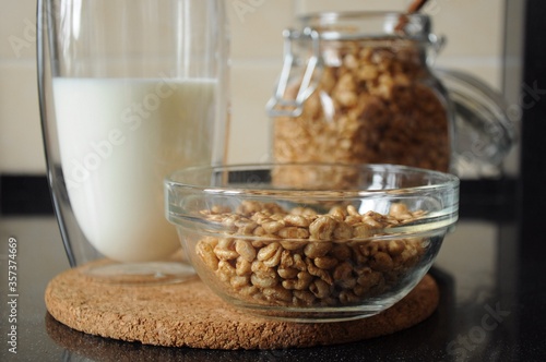 Breakfast from a bowl of wheat cereal, a glass of milk and a can of wheat cereal in the background on a cork stand