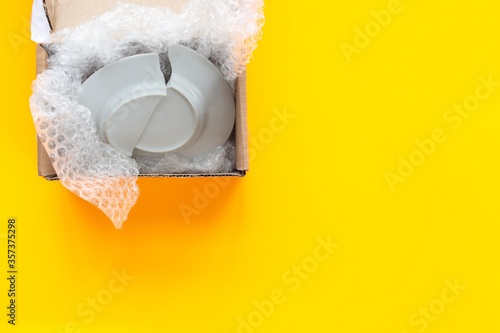 On a yellow background lies an open package, a box with a broken plate photo