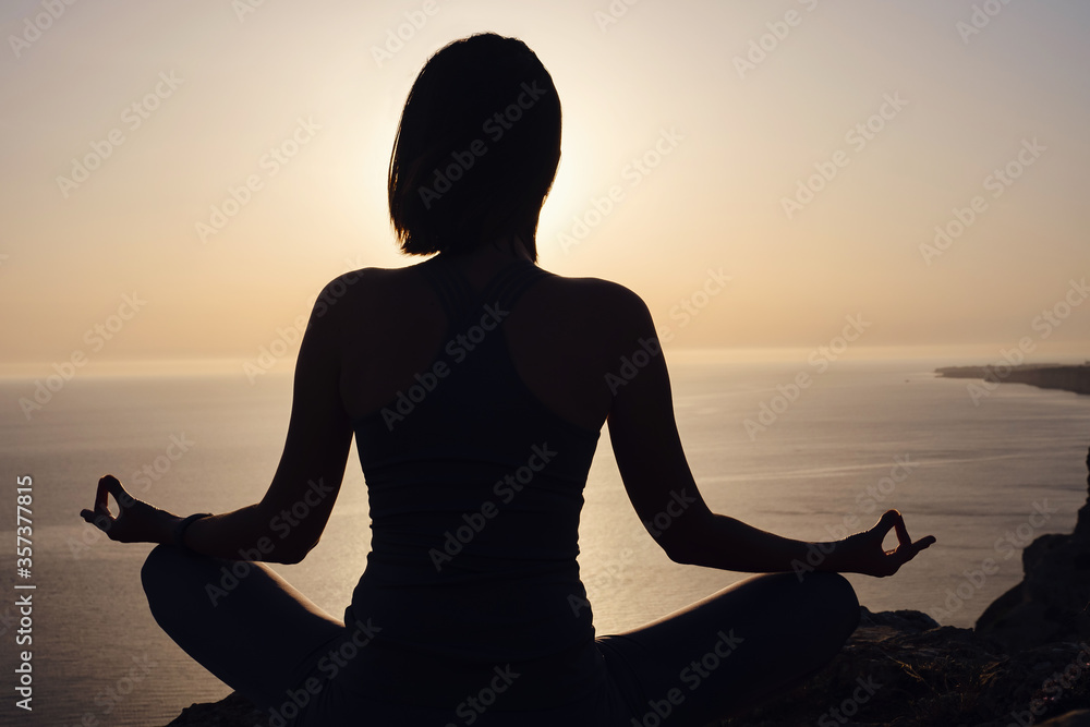 Young woman practicing yoga over sunset sea