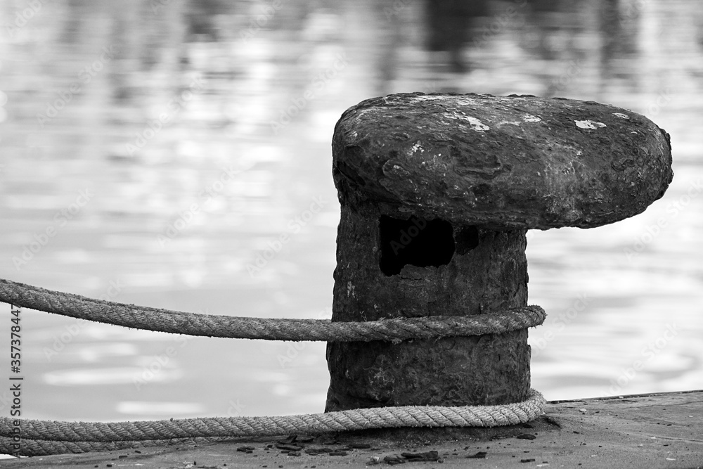 Fototapeta premium Grayscale shot of a rope curled over an old rusty metal pier