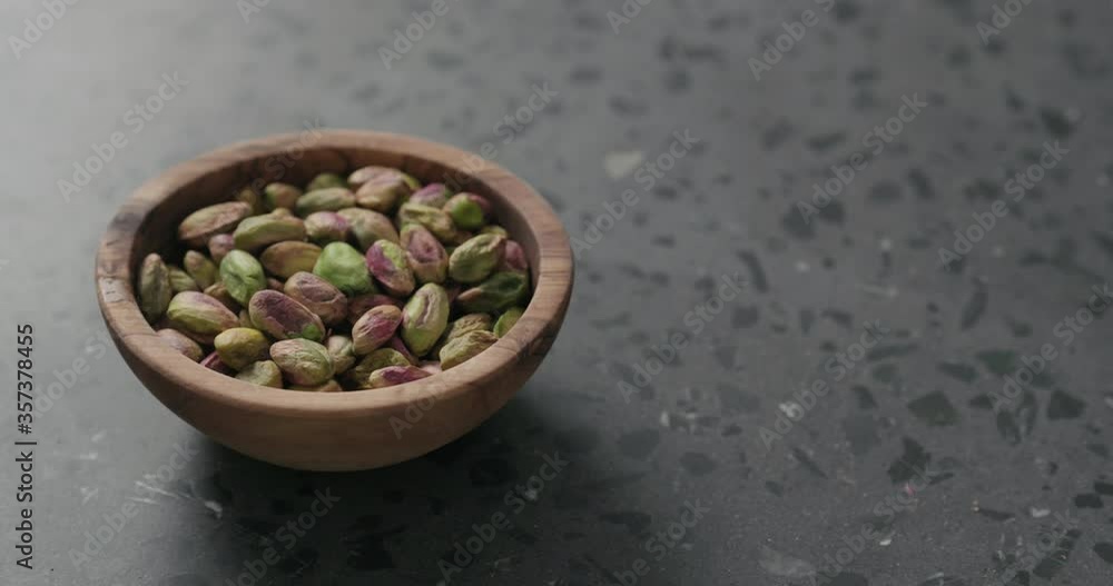 Handheld slow motion peeled pistachios in olive bowl on terrazzo surface Handheld slow motion peeled pistachios in olive bowl on terrazzo surface