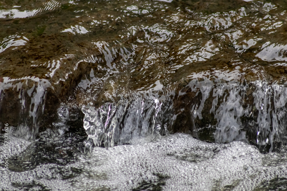 Calm floating creek with crystal clear water and rocks of a natural little dam or adventure hiking trail over a flat little brook in the woods as adventure tour for tourism with environmental health