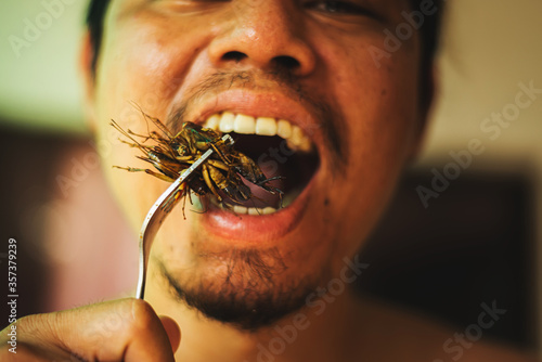 Asian young male eating cricket. Eating insect concept © yupachingping