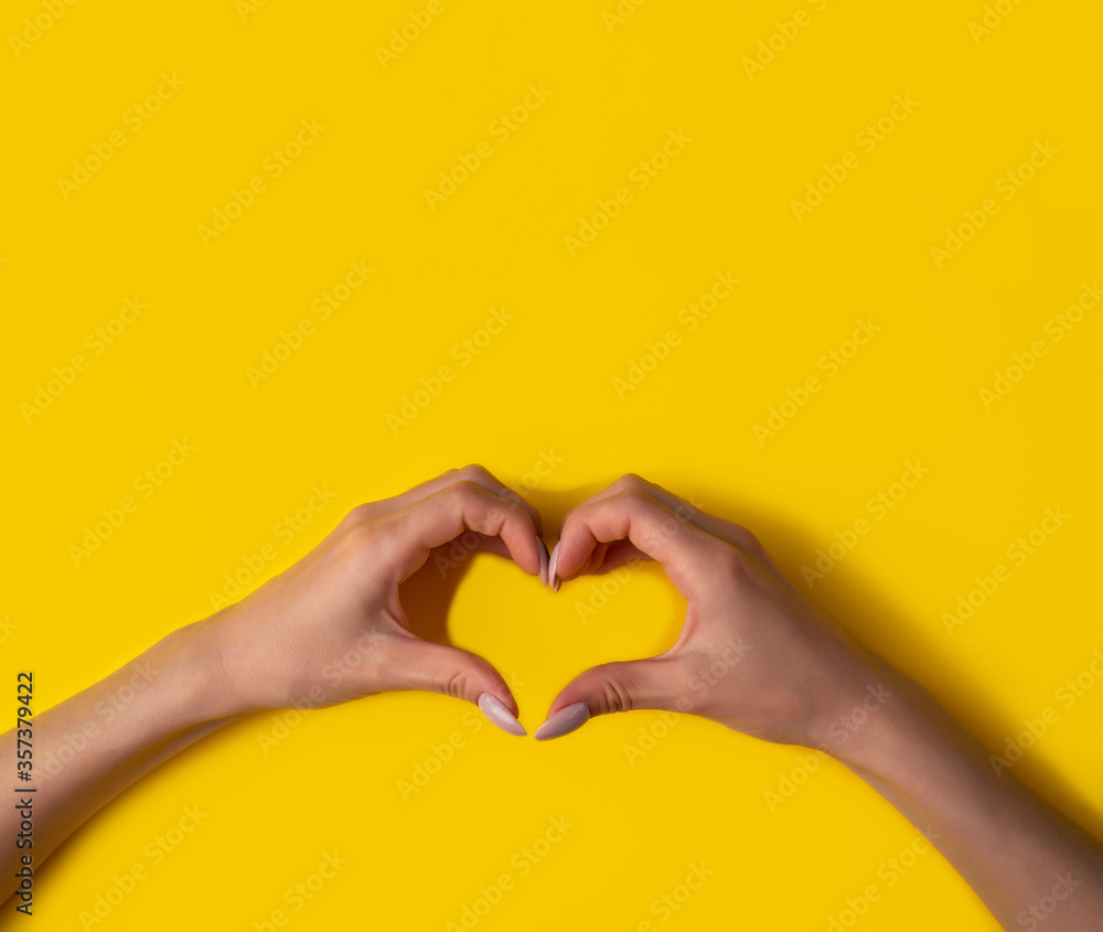 Obraz premium heart making woman's hands with manicure on yellow background, top view,banner