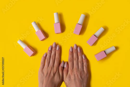 Gel polish of pink color and hands with manicure on a yellow background, top view