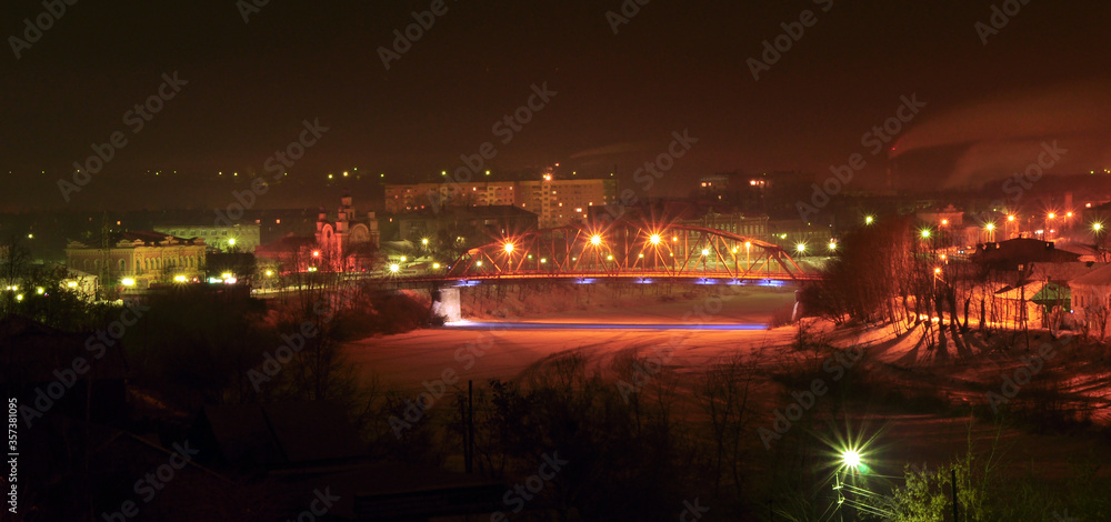 Night winter panorama of the city of Kungur. Road bridge over the frozen Sylva river.