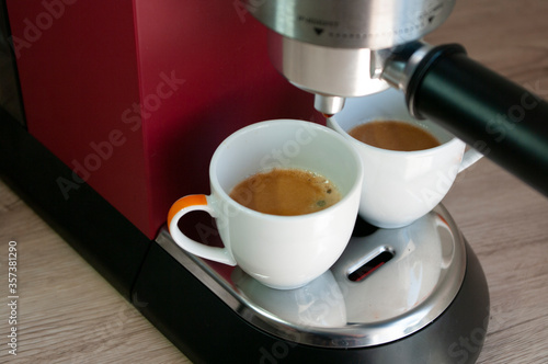 Two small cups with espresso coffee. Morning drink. Red coffee machine.