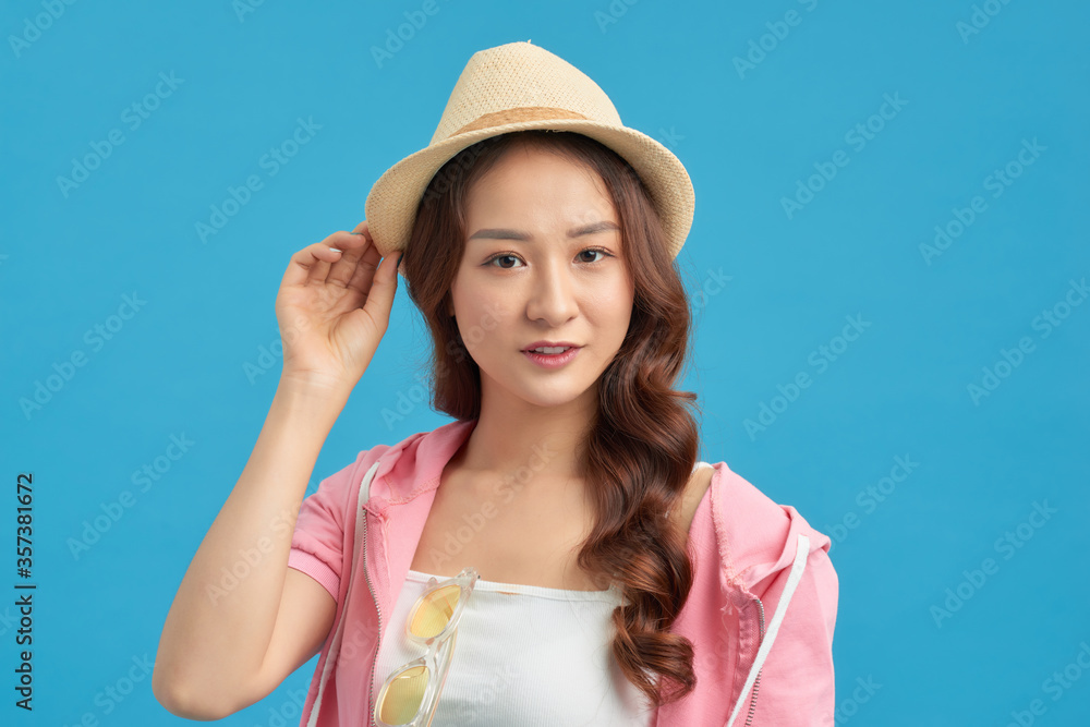 Beautiful young woman wearing summer straw hat posing against blue background