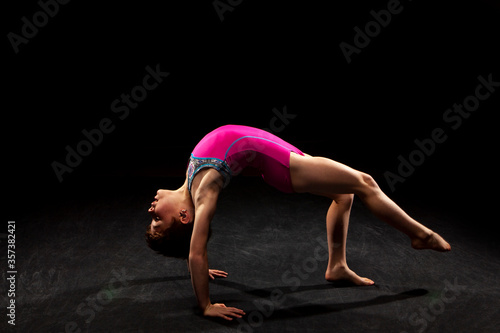 Young gymnast posing on a black background. 