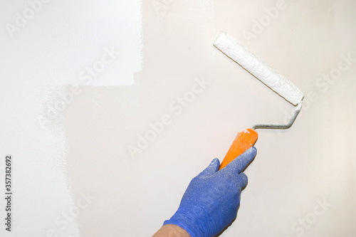 Repairs. A gloved hand holds a paint roller for painting the wall. Light streak. Real photo. Paint stained hand.