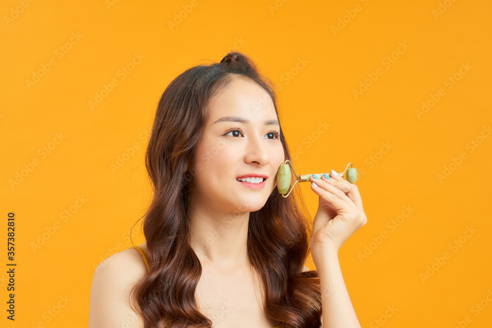 Beautiful Asian woman uses jade roller to massage her face Beautiful Asian woman uses jade roller to massage her face