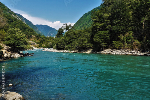 A river of aquamarine color flows between the slopes of the mountains covered with forest. The coast is rocky, the water is seething. Clouds on a bright blue sky. Abkhazia © Вера 