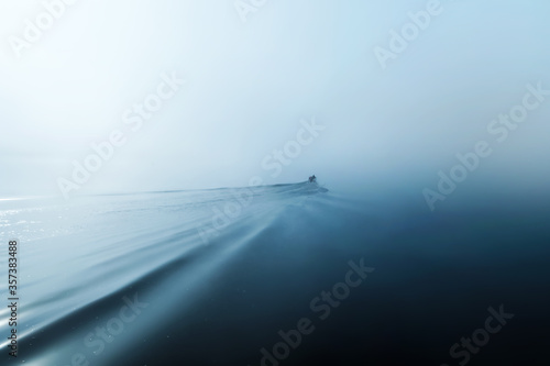 Motor boat at dawn sailing into the distance into the fog. Waveprint on the water