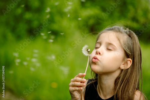 Summer in the park or forest. nature, freshness idea and freedom. happy childhood.Summer joy, little girl blowing dandelion at sunset near the river