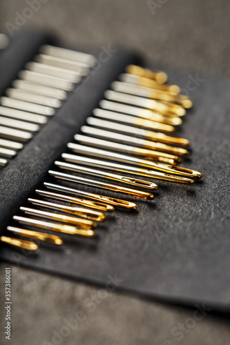 Gold sewing needles on a black background in a row.