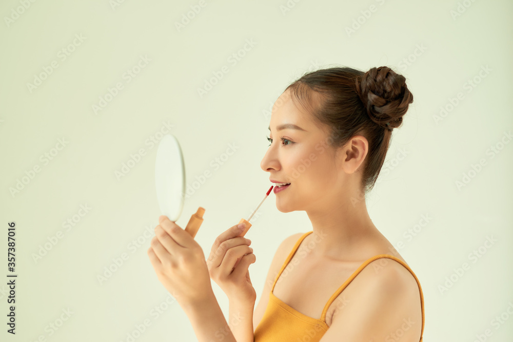 Portrait of young Asian woman applying lipstick and holding mirror isolated on light background. Portrait of young Asian woman applying lipstick and holding mirror isolated on light background.
