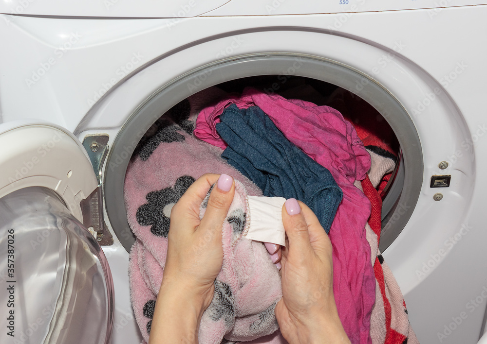 A woman looks at a clothing label. A washing machine drum full of dirty laundry in the bathroom. A woman looks at a clothing label. A washing machine drum full of dirty laundry in the bathroom.