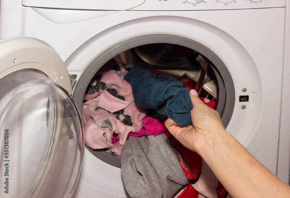 A woman takes out colored clothes from a washing machine. A washing machine drum full of dirty laundry in the bathroom.
