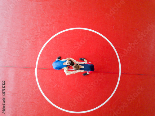 Aerial view of two wrestlers competing on a red wrestling mat. 