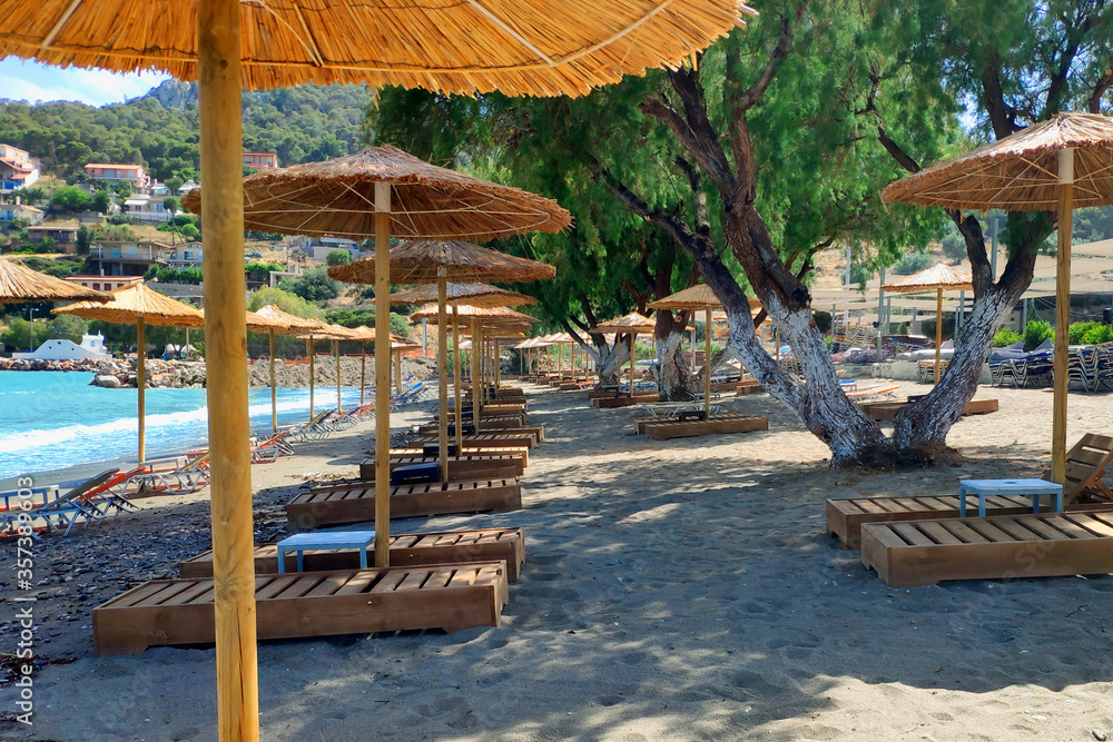 Naklejka premium Empty sun loungers without people under straw umbrellas on the beach.
