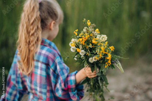 Little girl walking with bouquet of wildflowers, summer evening in countryside
