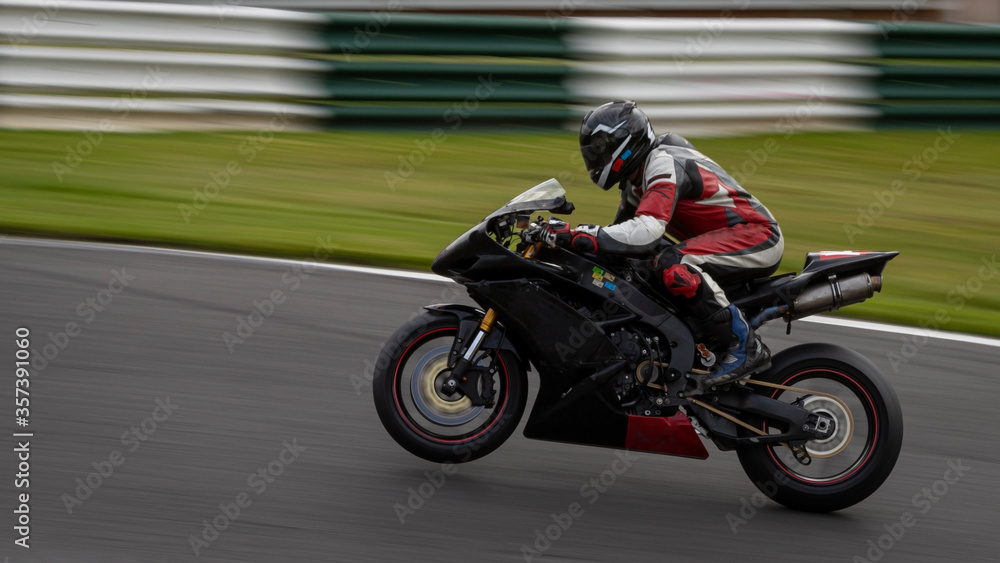 A panning shot of a black racing bike on one wheel as it circuits a track