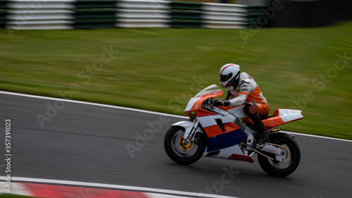 A panning shot of an orange and white racing bike as it circuits a track