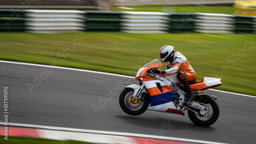 A panning shot of an orange and white racing bike on one wheel as it circuits a track © SnapstitchPhoto