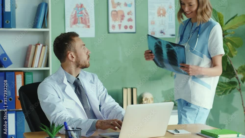Serious caucasian doctor working at the office on portable laptop. Daring young nurse flirting with therapist trying to seduce him. Sexual harrasment in the hospital. Problems. Serious caucasian doctor working at the office on portable laptop. Daring young nurse flirting with therapist trying to seduce him. Sexual harrasment in the hospital. Problems.