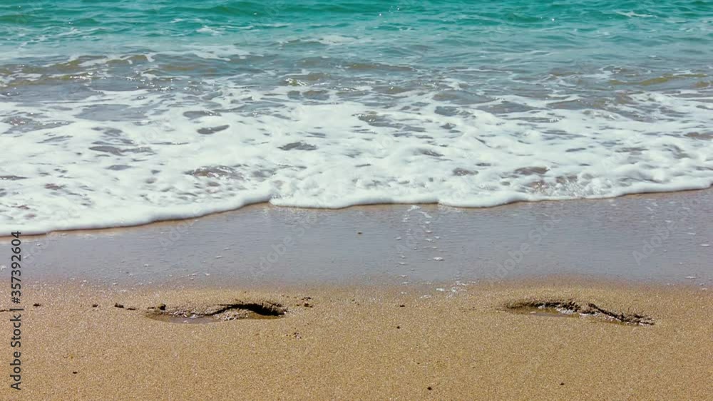 sea waves slowly wash away human footprints on the yellow sand sea waves slowly wash away human footprints on the yellow sand