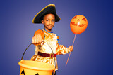 Serious portrait of a little boy with scary bucket for candies and in Halloween costume holding orange balloon