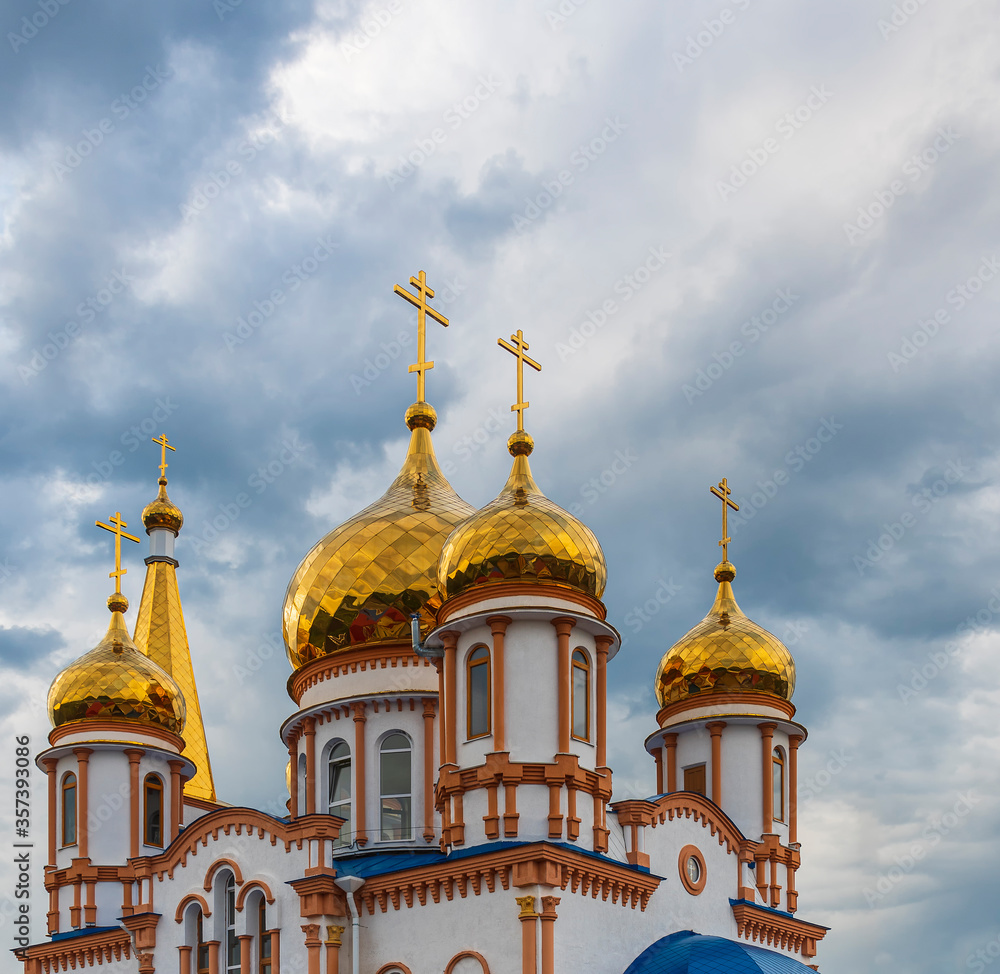 Golden domes of a snow-white Christian church against a disturbing cloudy blue summer sky