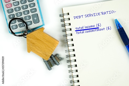 Conceptual image of debt service ratio for home loan repayment appraisal. Wooden key chain calculator notepad and pen in visibility. Focus on keychain.