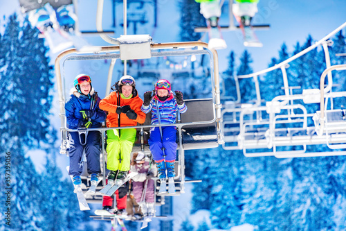 Three girls in colorful outfit sit on the ski lift talking and smiling together lifting on top of the mountain © Sergey Novikov