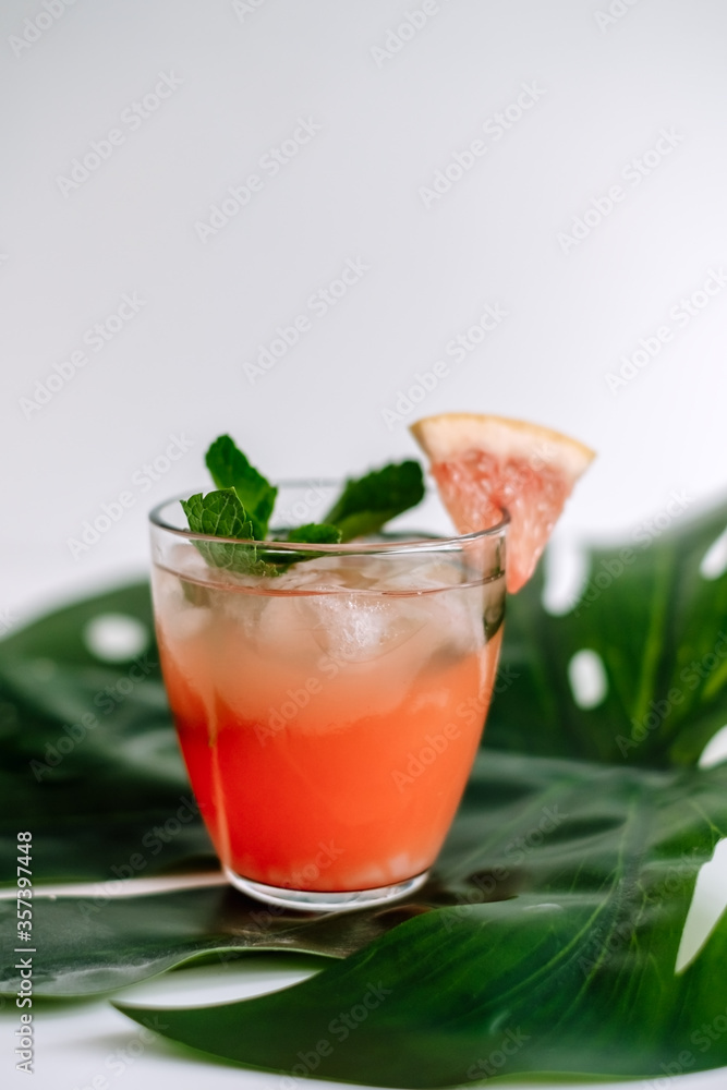 Grapefruit cocktail, lemonade with lime, mint and pieces of ice on a green tropical leaf. Grapefruit cocktail, lemonade with lime, mint and pieces of ice on a green tropical leaf.